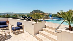 A rooftop pool area with a view of a mountain, a staircase, and outdoor seating.