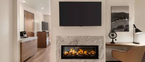 A modern living room with a fireplace, a flat-screen TV, and a dining area with a wooden table and chair.