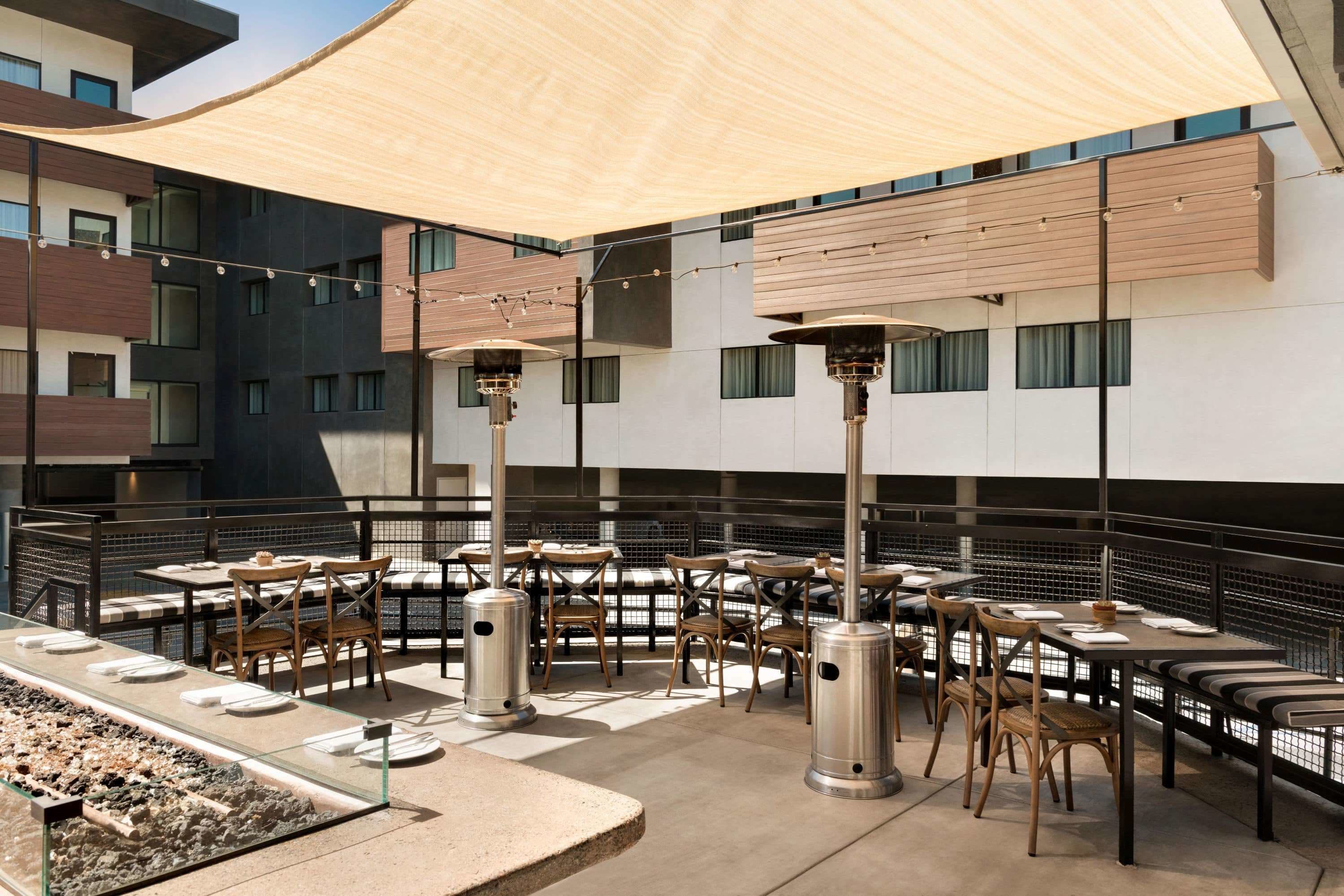 An outdoor dining area with tables and chairs, a fire feature, and a large canopy.