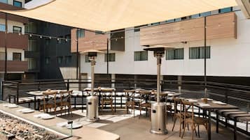 An outdoor dining area with tables and chairs, a fire feature, and a large canopy.