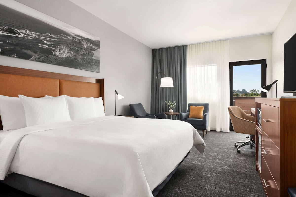 A hotel room with a large bed, a desk, a chair, a TV, and a window with a view.
