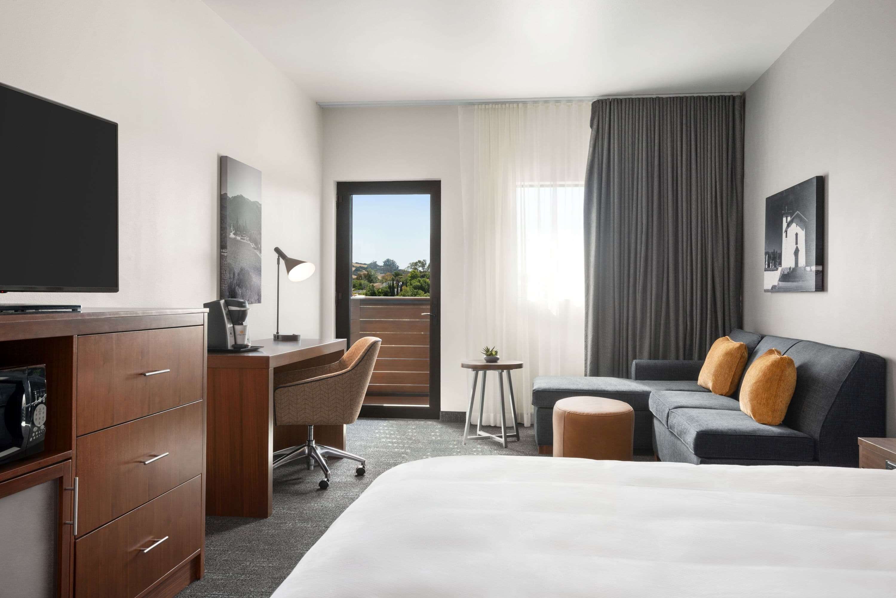 A hotel room with a bed, a desk, a chair, a sofa, and a TV.