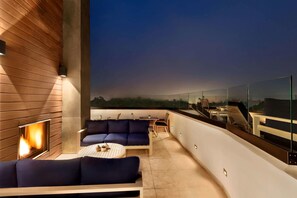 A modern outdoor lounge area with a fireplace, seating, and a glass railing overlooking a cityscape. - La Quinta Inn & Suites by Wyndham San Luis Obispo Downtown (San Luis Obispo)