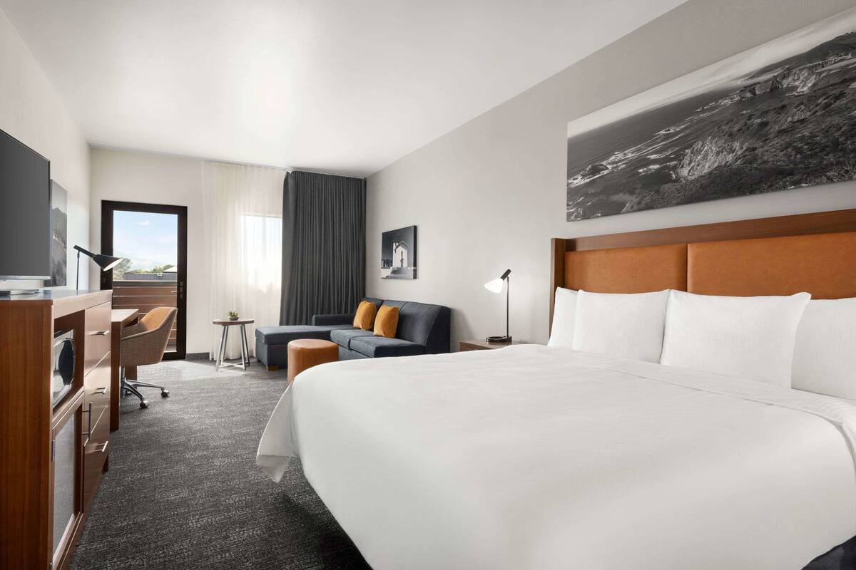 A hotel room with a large bed, a desk with a chair, a sofa, a small table, and a large window.