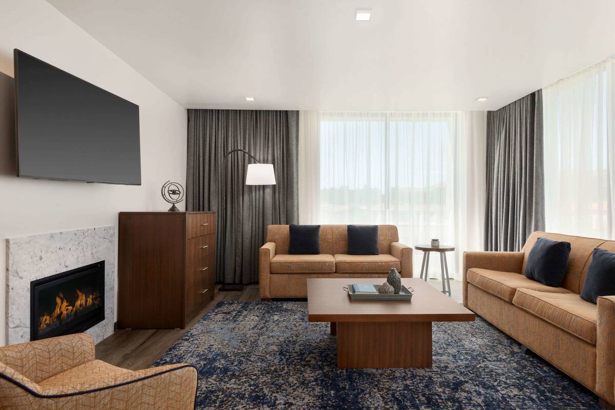 A modern living room with a flat-screen TV, a fireplace, a sofa set, a coffee table, and a patterned rug.