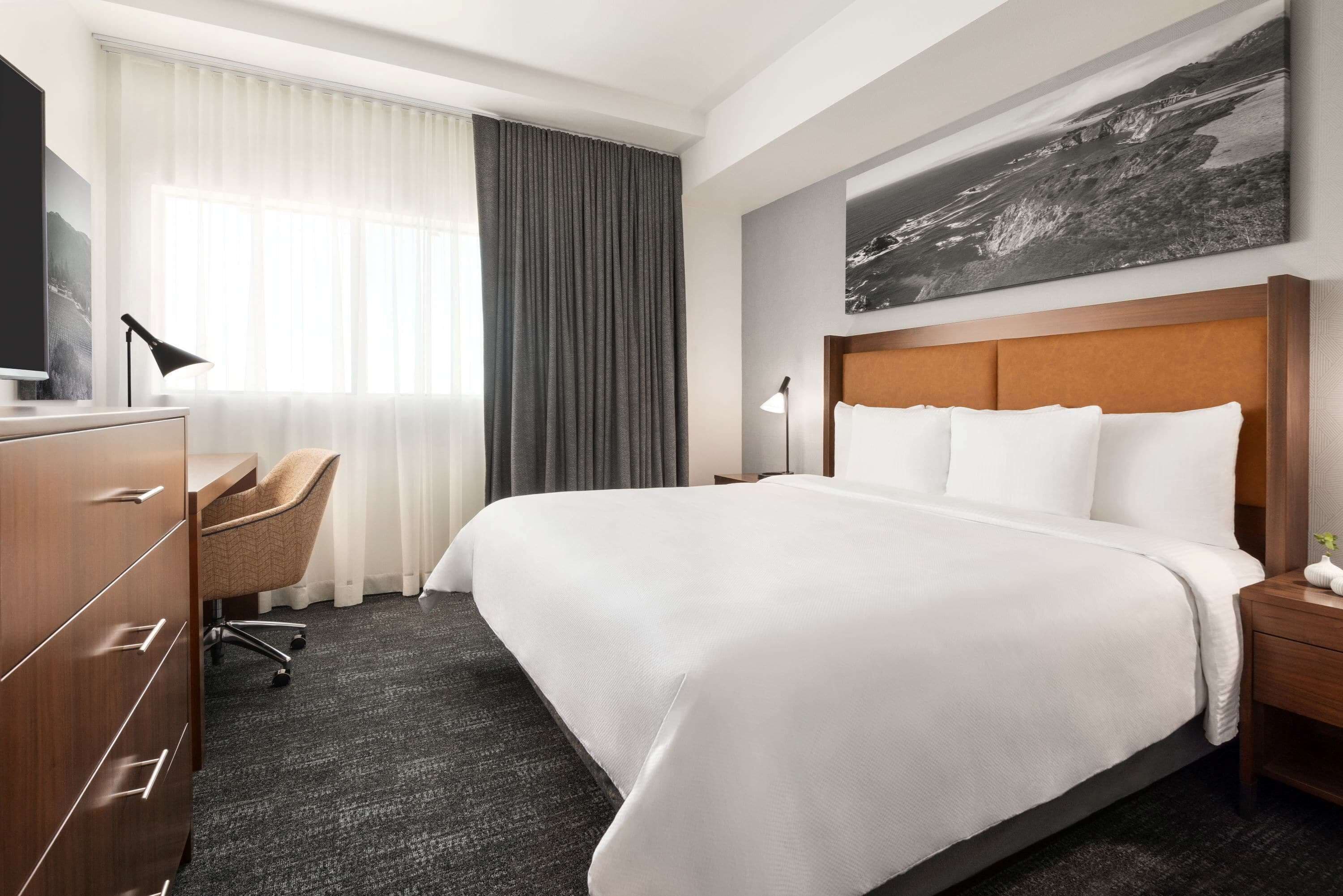 Een hotelkamer met een groot bed, een bureau met stoel, een kledingkast en een schilderij aan de muur.
