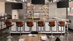 A modern bar area with a central counter, bar stools, and shelves stocked with bottles and glasses.