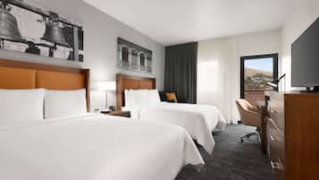 A hotel room with two beds, a desk, a TV, and a large window with a view.