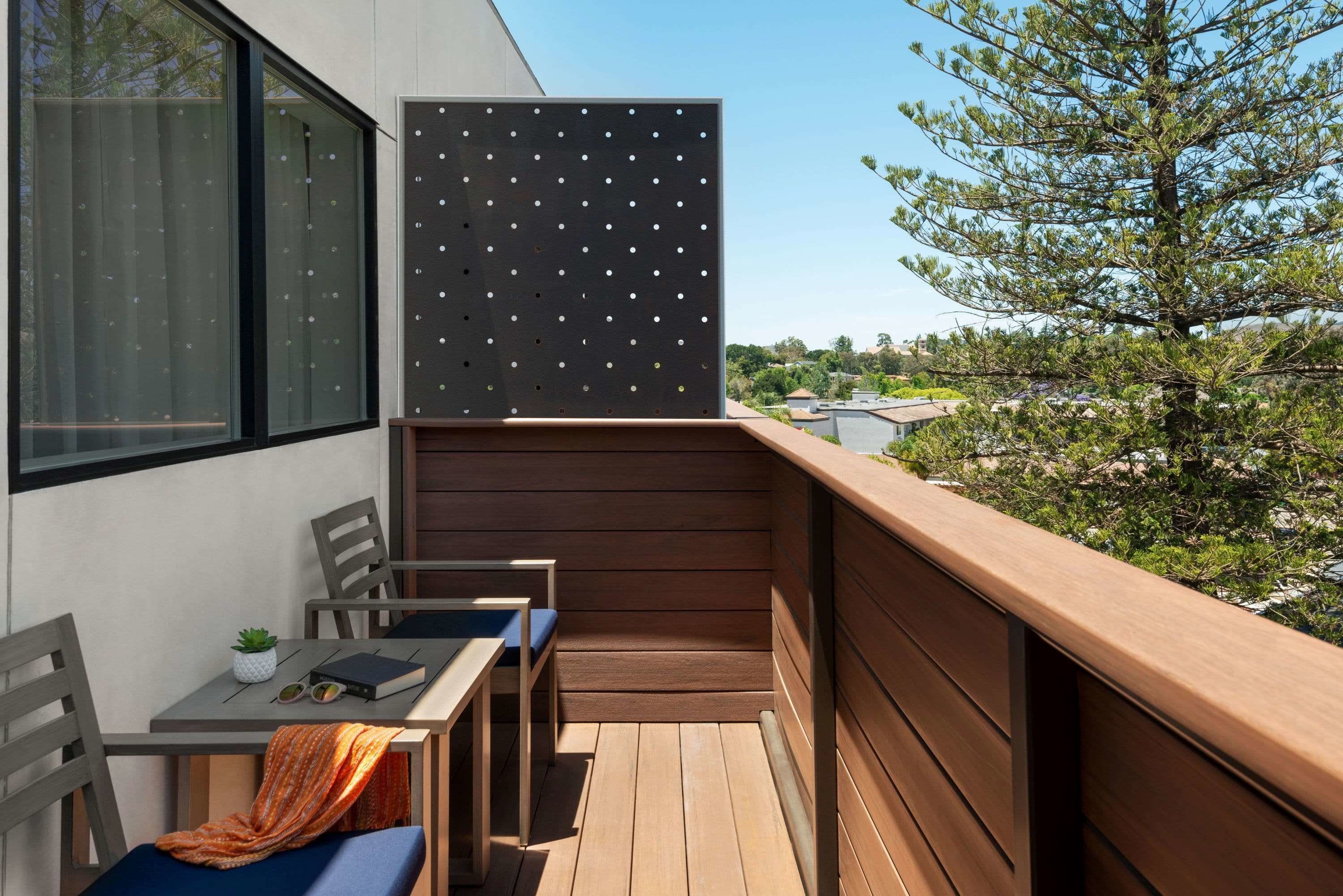 A balcony with a table, chairs, and a view of trees and buildings.