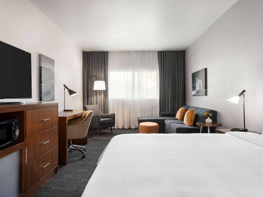 A hotel room with a bed, a desk, a chair, a television, and a window with curtains.