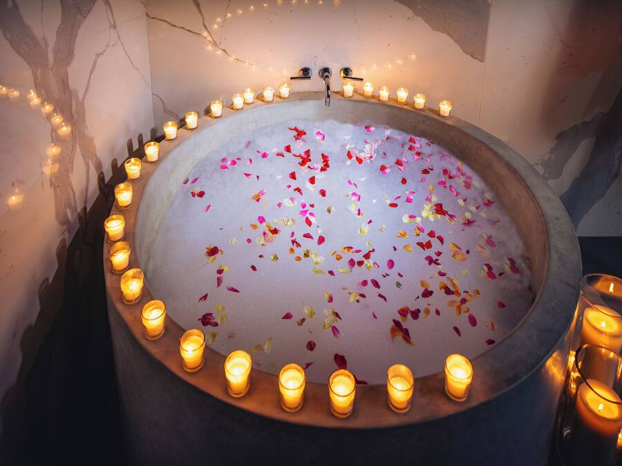 A bathtub surrounded by candles and flower petals.