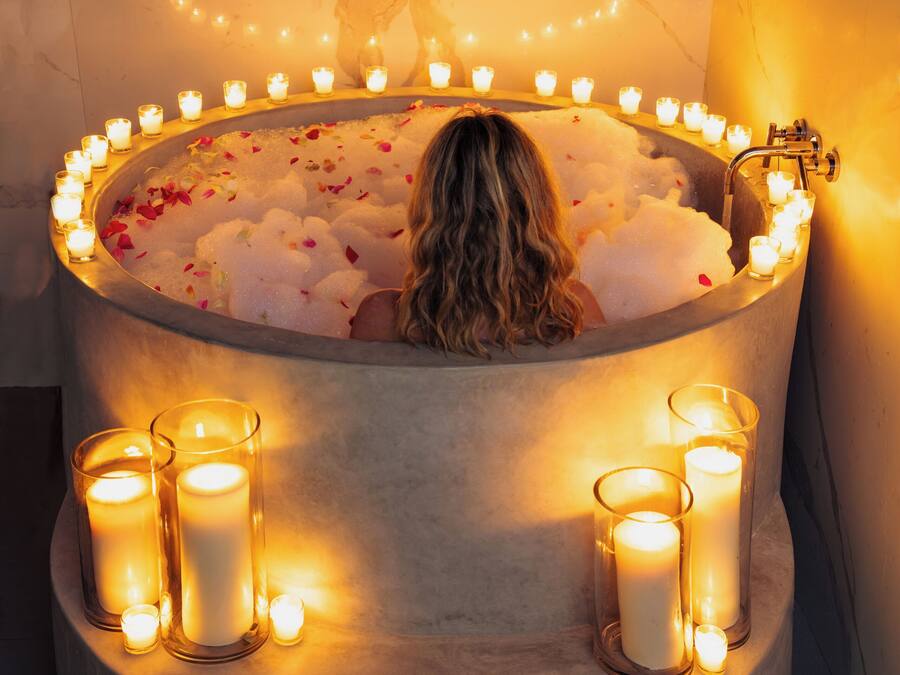 A bathtub surrounded by candles, with a tree mural on the wall.
