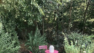 Un jardín con una mesa y sillas, rodeado de abundante follaje.