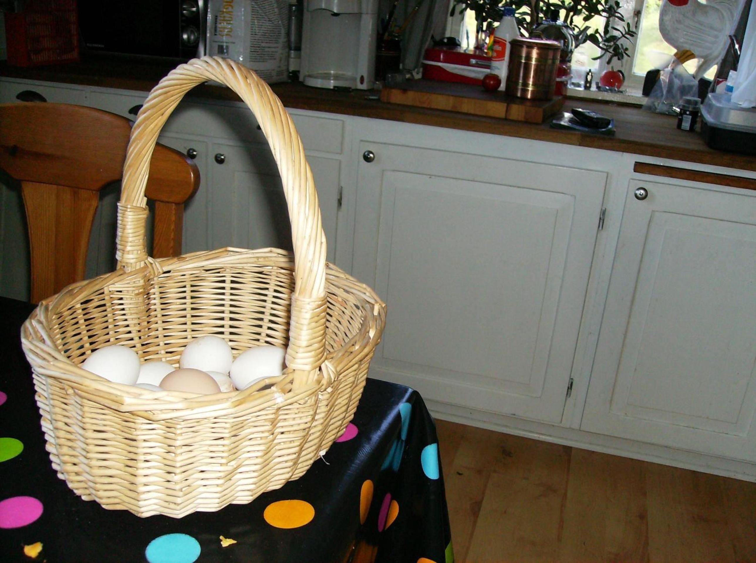 A wicker basket with eggs on a table with a polka dot tablecloth.