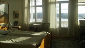 A bedroom with a bed, a desk, a chair, a window with curtains, and a view of a snowy landscape. - Täljegården Lantgårdshotell (Erikslund)