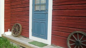 A red wooden house with a blue door, a small porch, and two old-fashioned wheels. - Täljegården Lantgårdshotell (Erikslund)