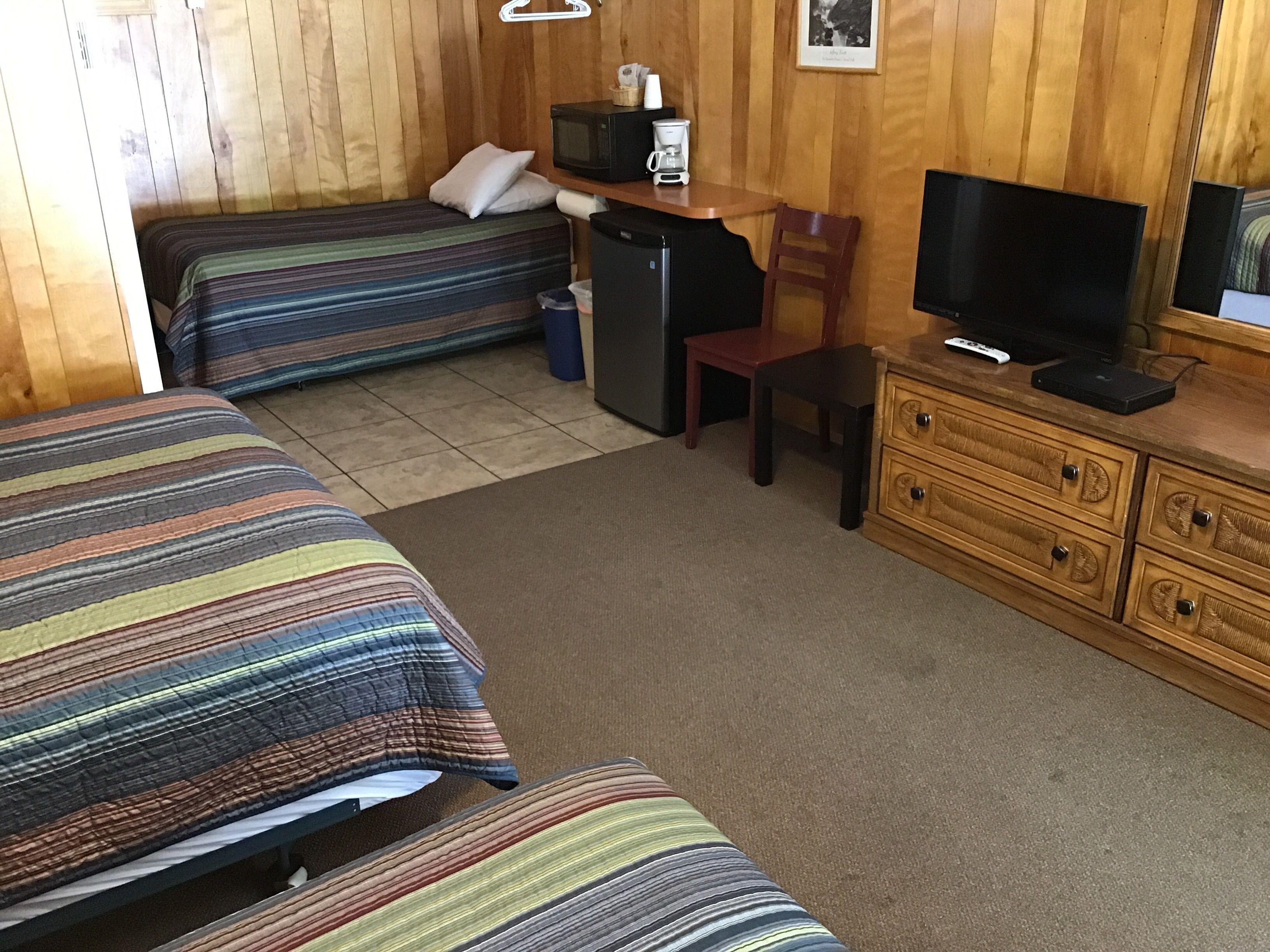Una camera con due letti, un piccolo frigorifero, una televisione e un comò in legno.