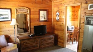 Een houten kamer met een televisie op een dressoir, een spiegel en een eethoek met een tafel en stoelen.