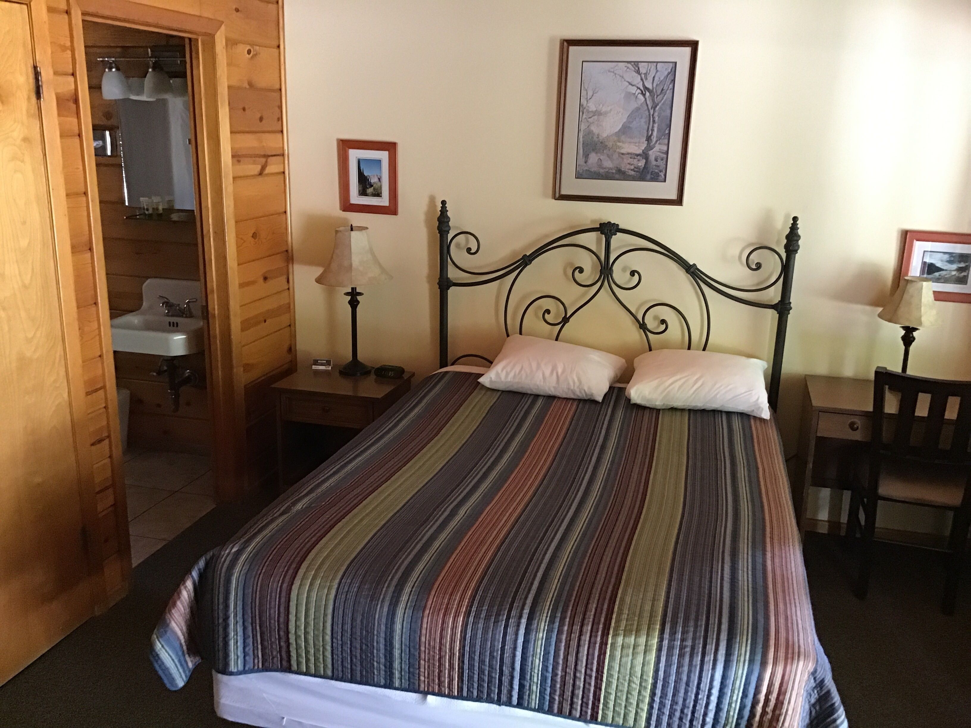 Un dormitorio con cama, armario de madera, mesita de noche con lámpara y un cuadro enmarcado en la pared.