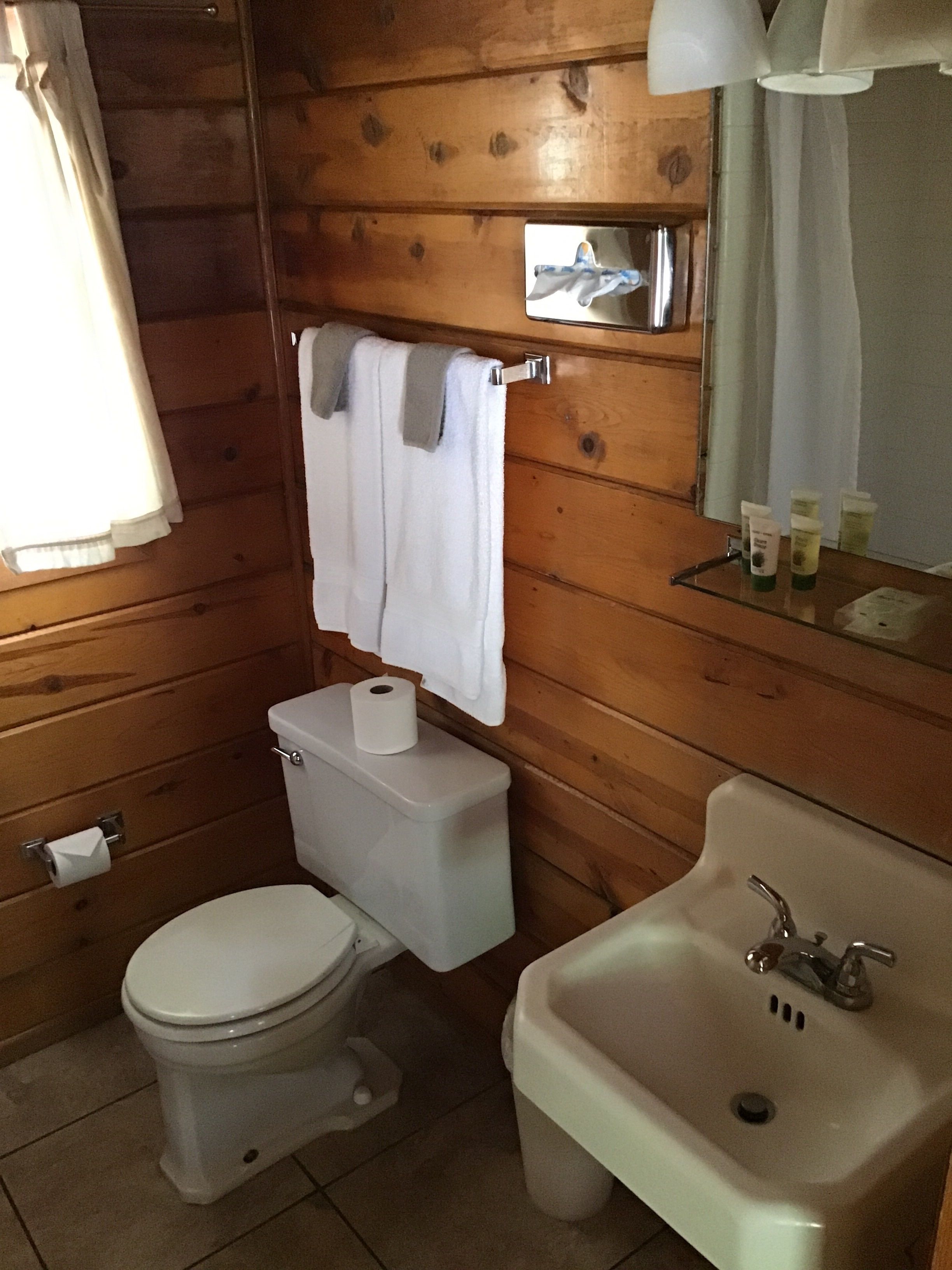 A wooden-paneled bathroom with a toilet, sink, and a towel hanging on a rack.