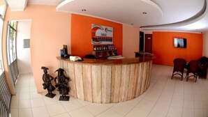 A reception area with a curved counter, a sign for 'TARIFAS', and a television mounted on the wall. - Hotel Itaparica (Caruaru)