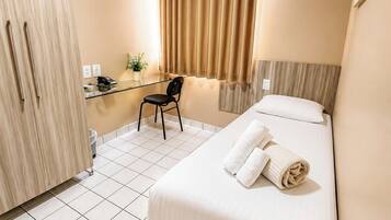 A hotel room with a bed, a desk, a chair, a wardrobe, and an air conditioning unit.