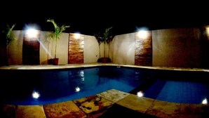 A nighttime swimming pool with tiled flooring and potted plants along the walls. - Hotel Itaparica (Caruaru)