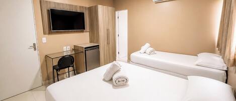 Habitación de hotel con cama, escritorio, silla, televisor y aire acondicionado.