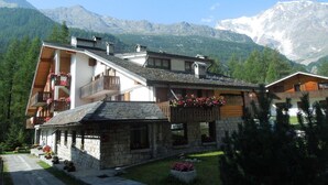 A mountain lodge with stone and wooden structures, balconies with flower boxes, and a view of snow-capped mountains. - Residence Weissthor (Macugnaga)