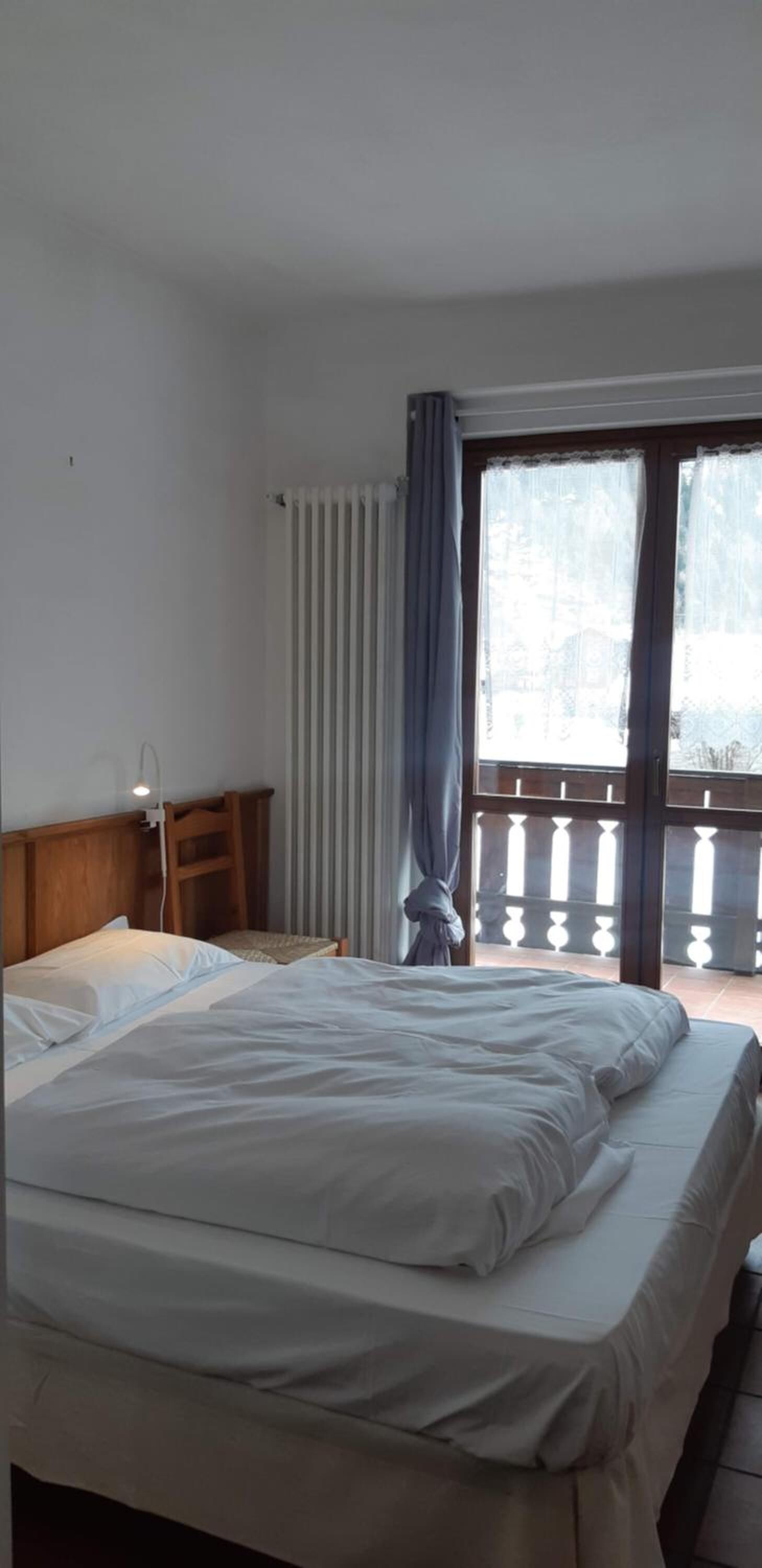 A bedroom with a bed, a nightstand, a window with curtains, and a view of the outside.