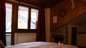 A cozy room with a bed, a fireplace, and a window with curtains. - Residence Weissthor (Macugnaga)