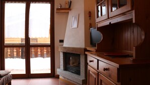 A cozy living room with a fireplace, wooden cabinets, and a sliding glass door leading to a balcony. - Residence Weissthor (Macugnaga)
