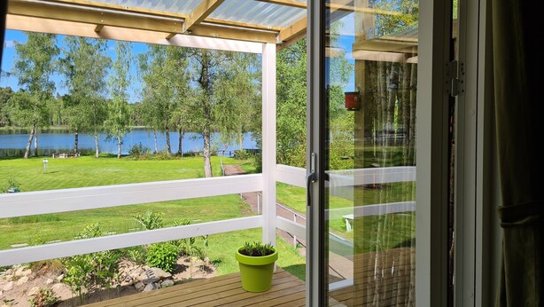 A covered outdoor area with a view of a lake and trees. - Den Sovande Älgen (Markaryd)