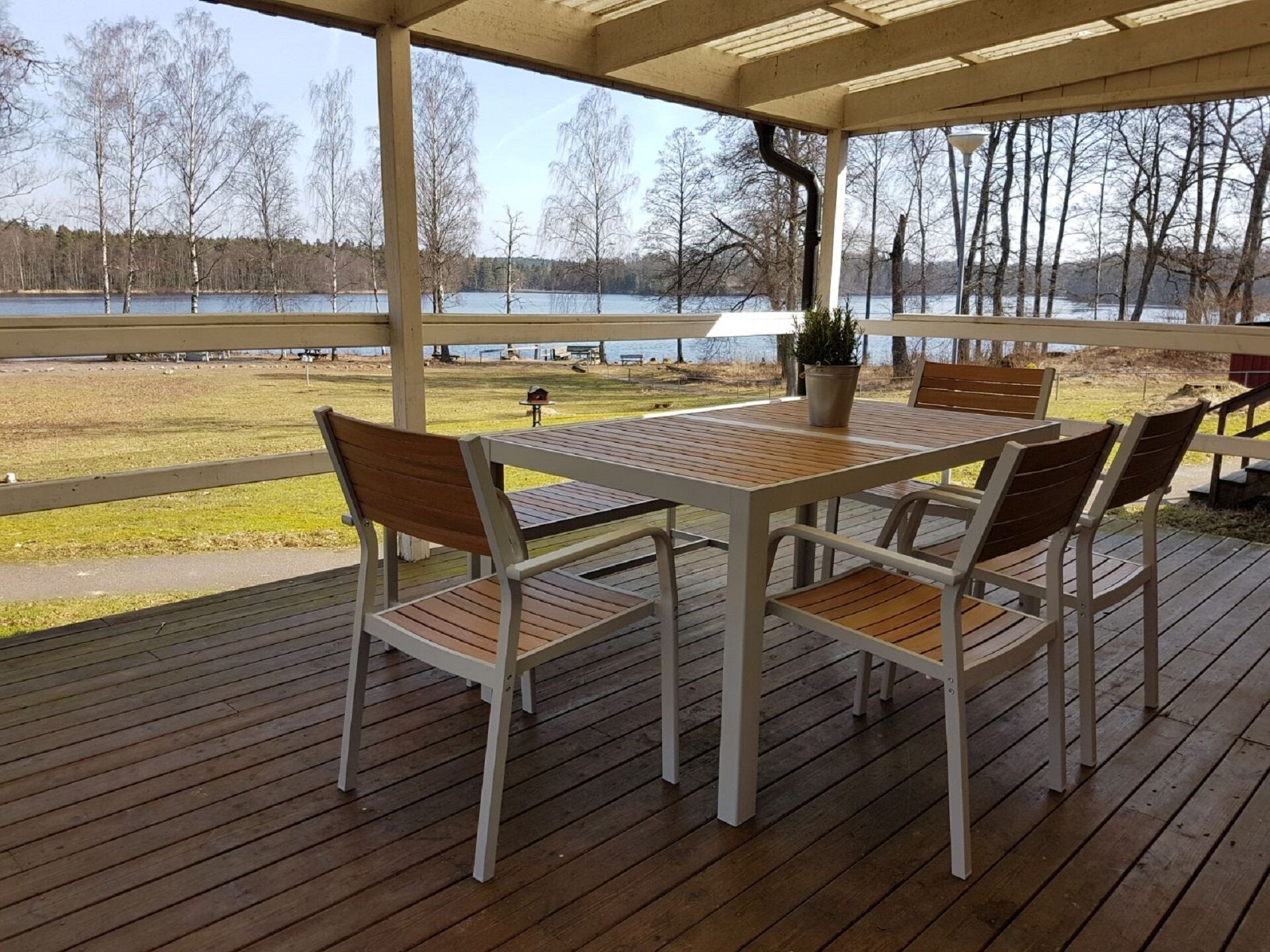 A covered outdoor deck with a table and chairs, overlooking a lake and trees.