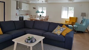 A modern living room with a dark blue sectional sofa, a white coffee table, and a dining area with a wooden table and chairs. - Den Sovande Älgen (Markaryd)