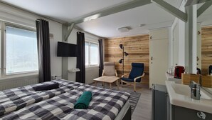 A hotel room with a bed, a desk with a mirror, a chair, a TV mounted on the wall, and a wooden wall panel. - Den Sovande Älgen (Markaryd)