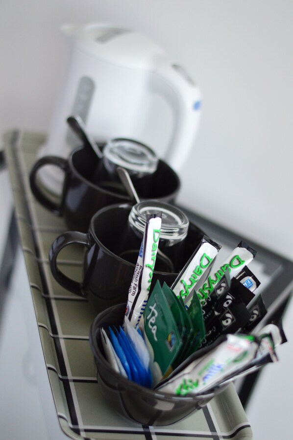 A kitchen shelf with black mugs, a white kettle, and various packaged food items.