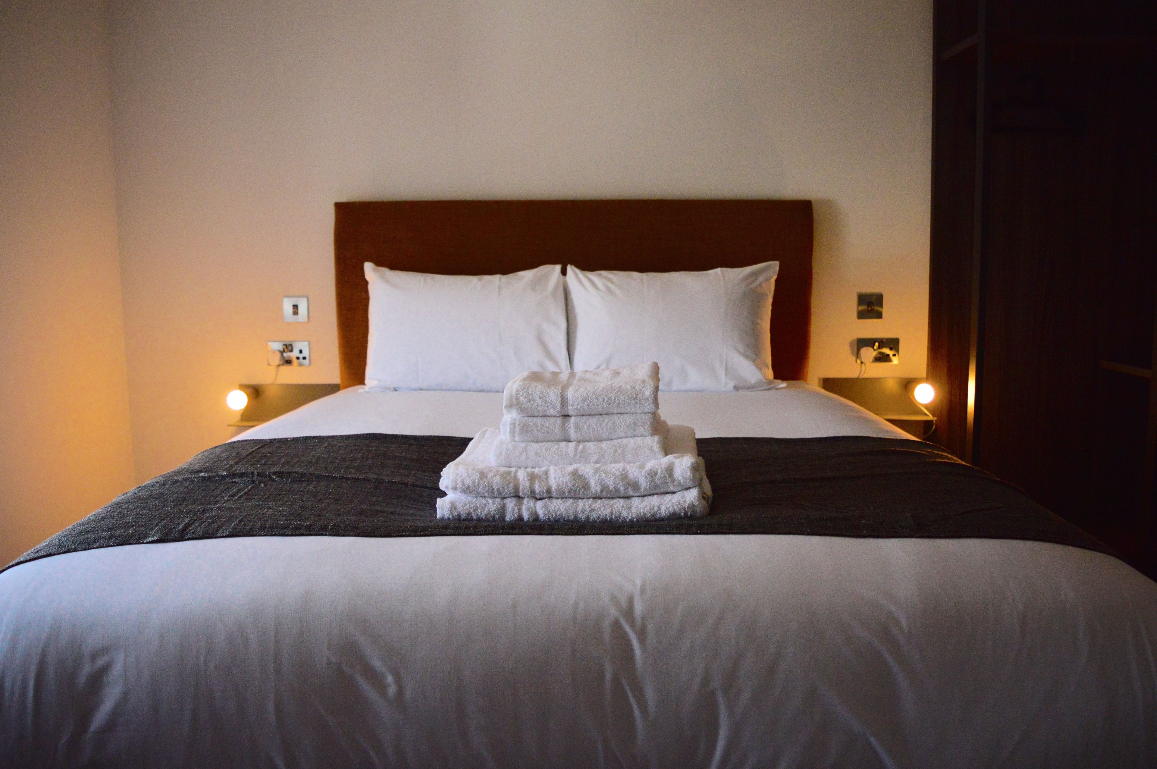 A neatly made bed with white linens and a folded towel on the bed.