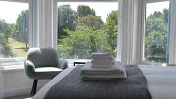 Quarto de hotel com uma cama grande, uma cadeira e vista para um campo de golfe pelas janelas.
