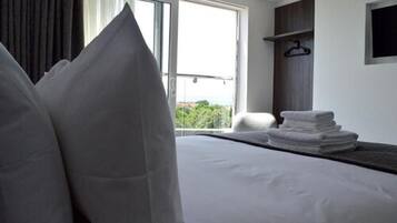 A hotel room with a bed, pillows, a window with a view, and a stack of towels.