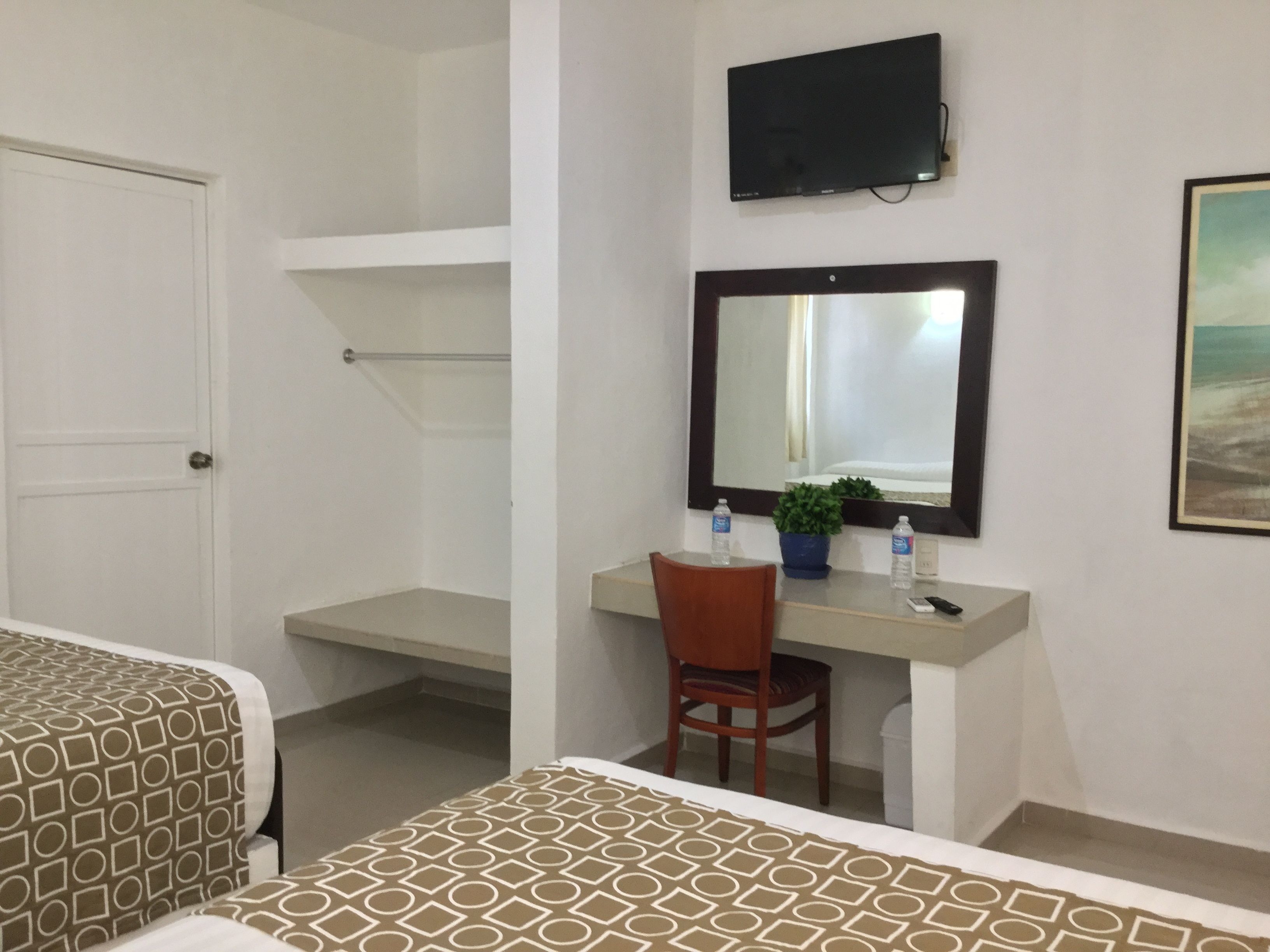 A hotel room with a bed, a desk with a chair, a television mounted on the wall, and a painting on the wall.