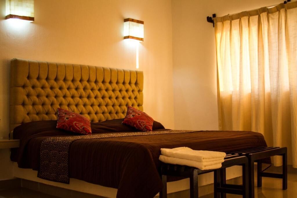 A neatly made bed with a tufted headboard, two pillows, and a bedside table with a folded towel.