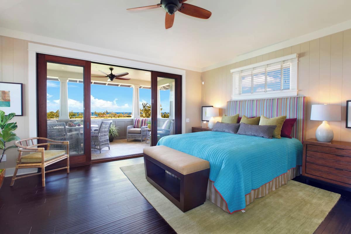 Ein Schlafzimmer mit einem großen Bett, einem Deckenventilator, einer Glasschiebetür, die auf einen Balkon führt, und Meerblick.
