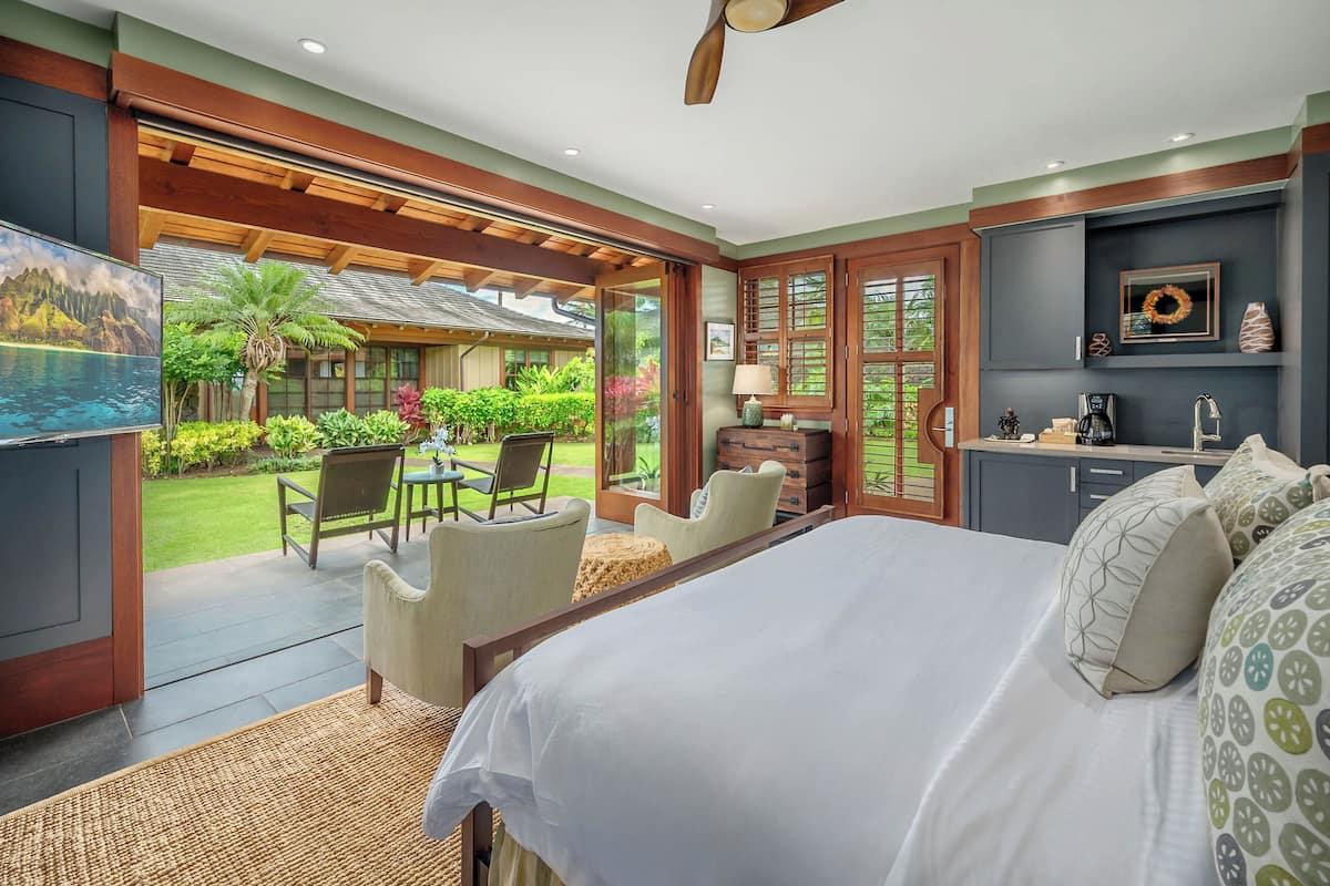 Ein Schlafzimmer mit Bett, Schreibtisch und Stuhl. Blick auf einen Garten und ein Schwimmbad.
