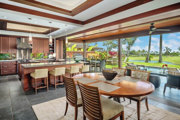 A modern kitchen with a large island, bar seating, and a view of a lush garden and pool.