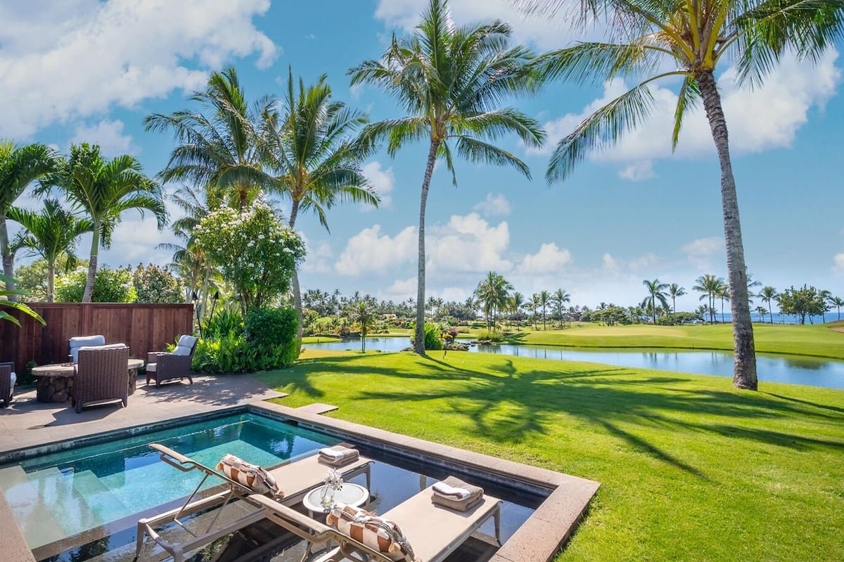 Ein Poolbereich mit Liegestühlen, einer Holzlattenumzäunung und Blick auf einen Golfplatz und ein Gewässer.
