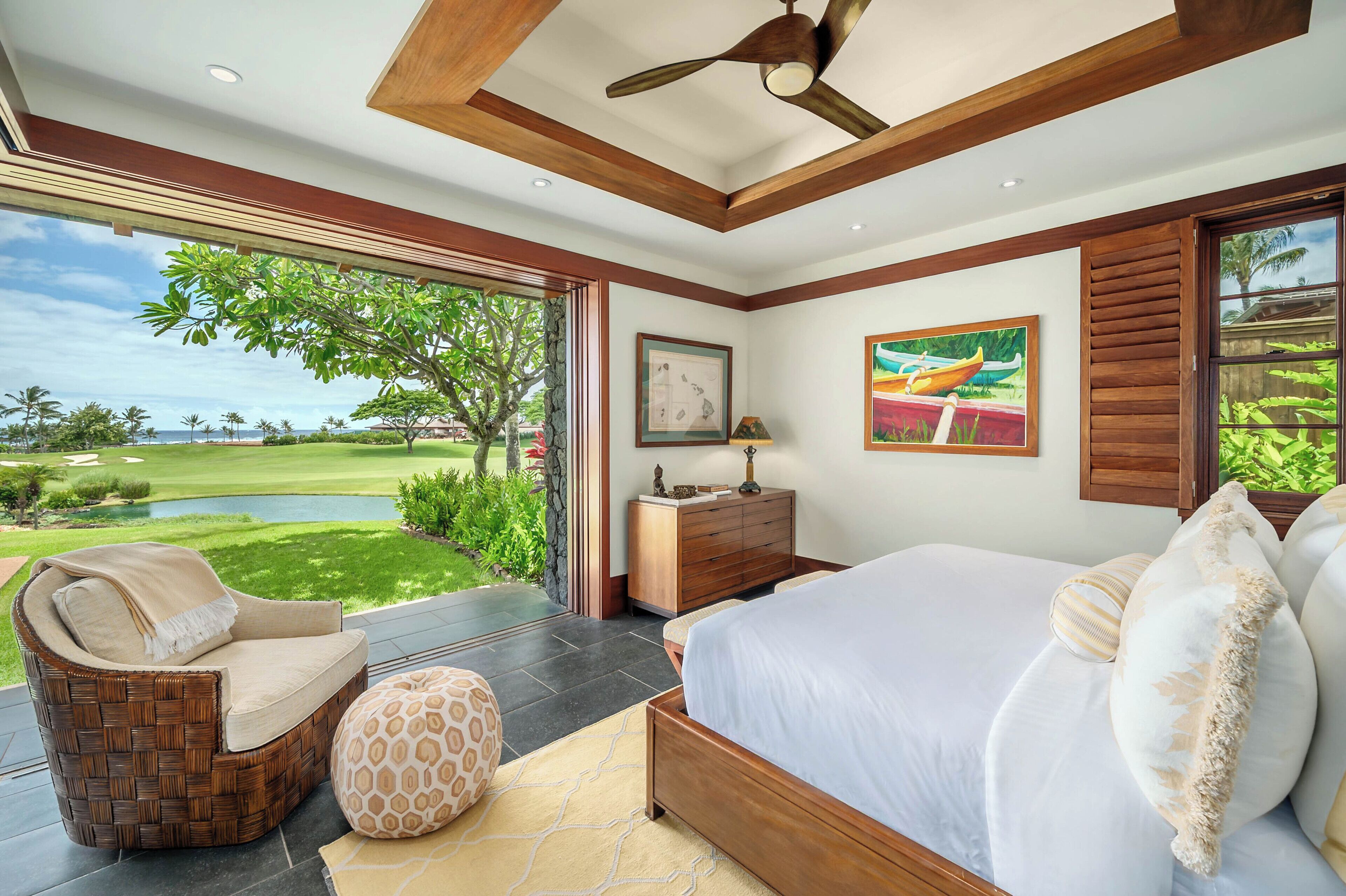A bedroom with a large bed, a chair, a nightstand, and a view of a golf course.