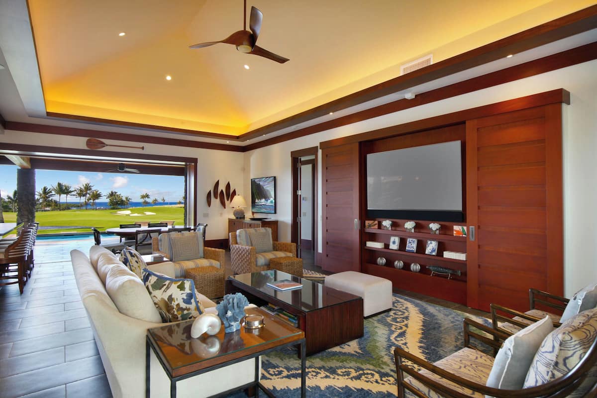 Ein geräumiges Wohnzimmer mit großem Fernseher, bequemen Sitzmöglichkeiten, einem Couchtisch und Blick auf einen Golfplatz.