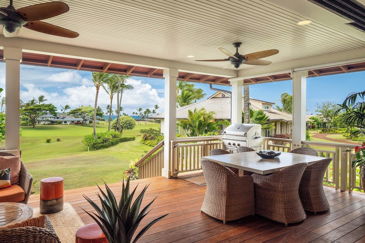 Ein überdachter Außenbereich mit Tisch und Stühlen, einem Deckenventilator und Blick auf einen Golfplatz.