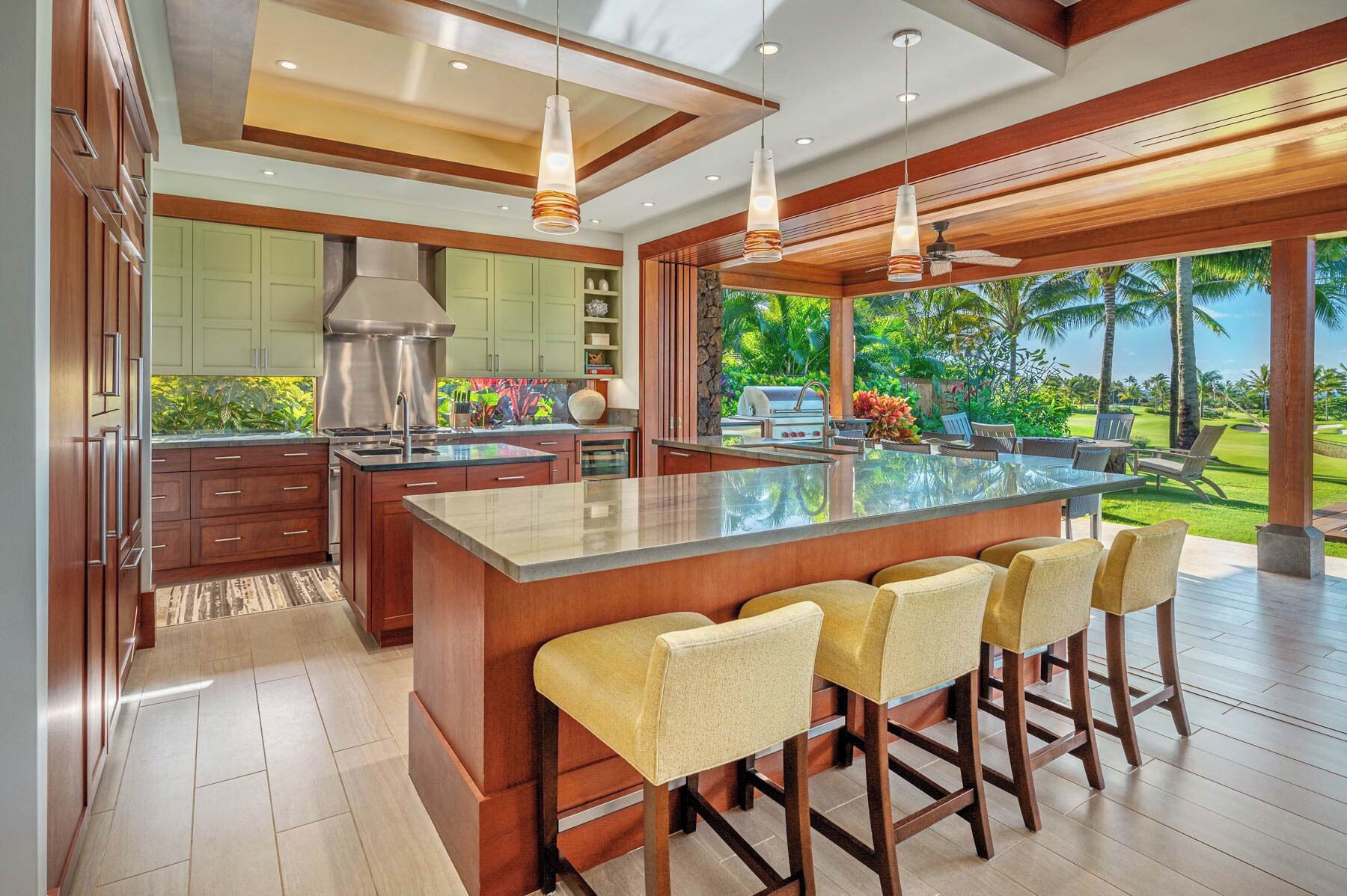 A modern kitchen with a large island, bar stools, and a view of a tropical garden.